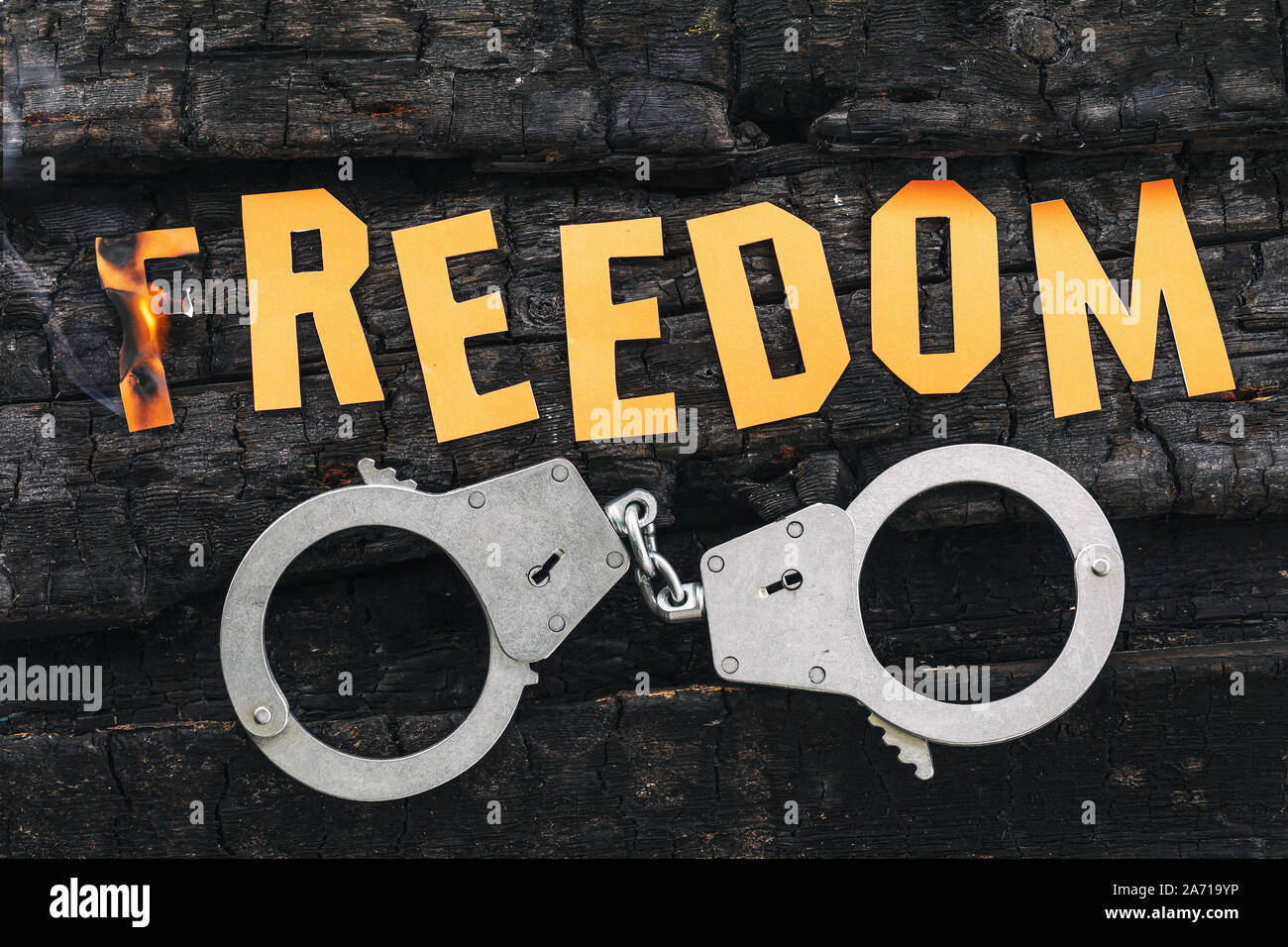 Freedom is in danger. Burning letters made of paper and handcuffs lying nearby on charred boards. Justice concept Stock Photo