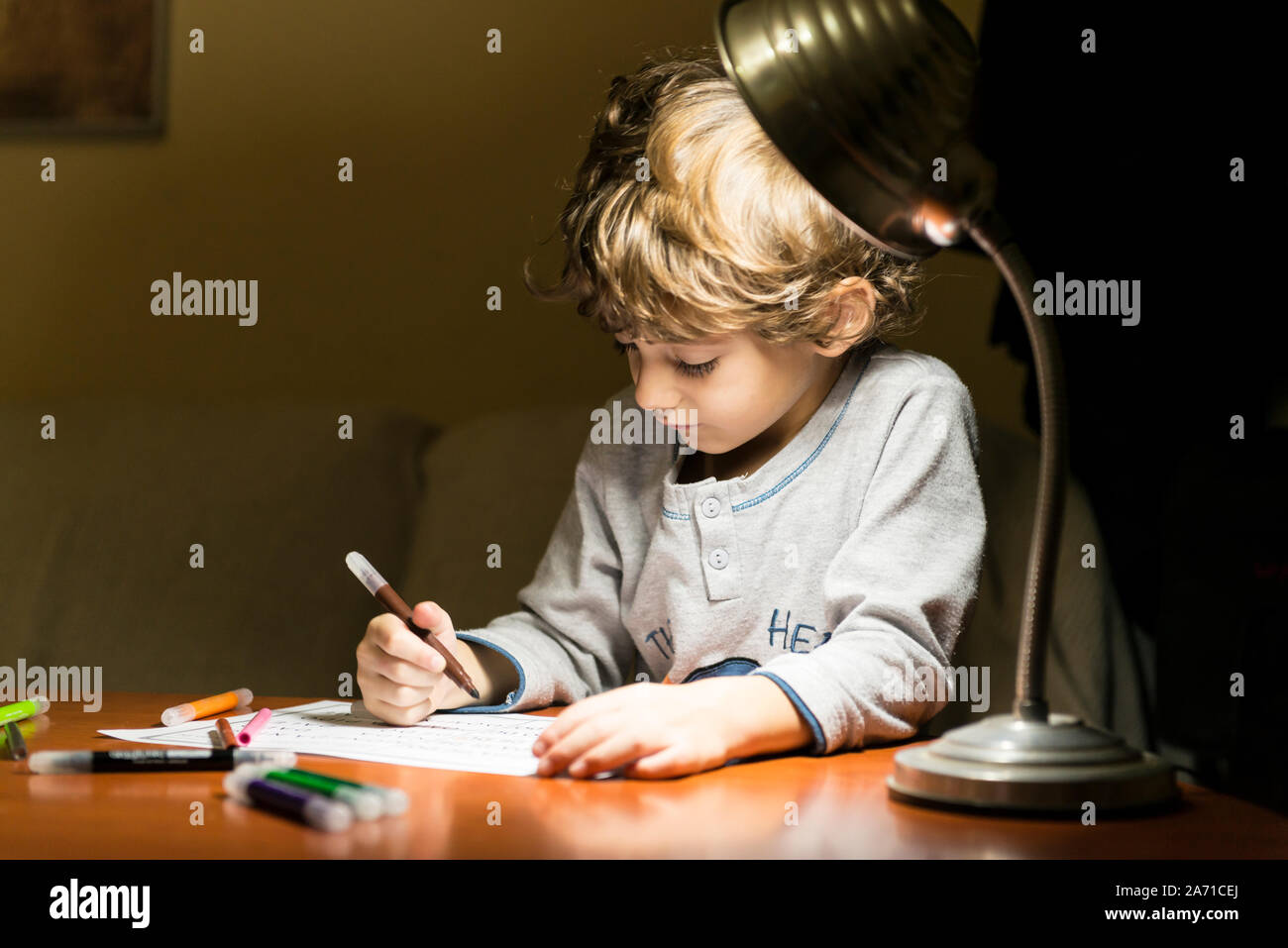 Child drawing with markers, illuminated by the light of a lamp. Stock Photo