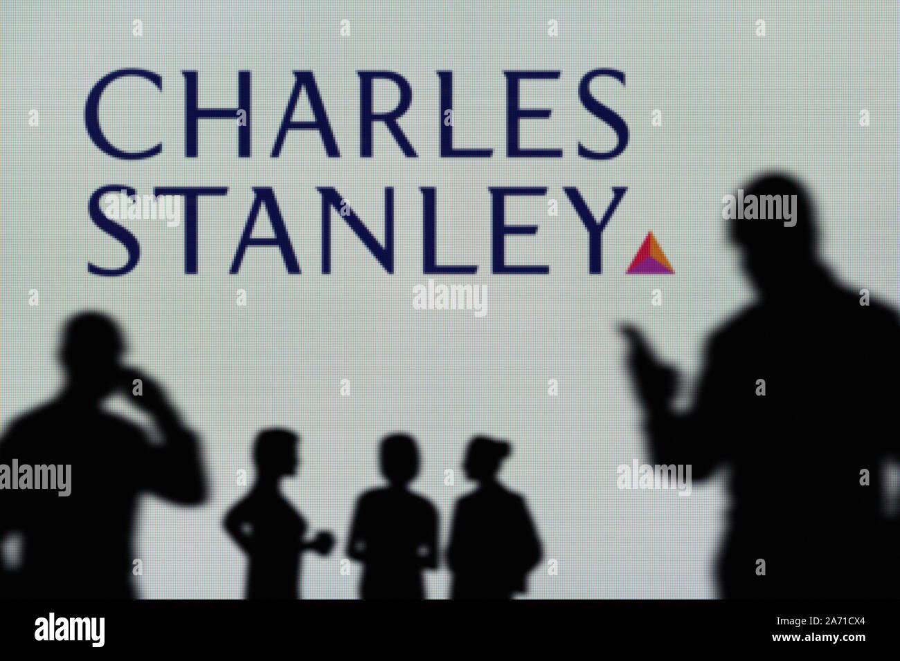 The Charles Stanley logo is seen on an LED screen in the background while a silhouetted person uses a smartphone (Editorial use only) Stock Photo