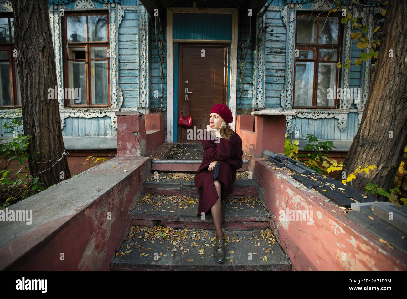 Woman in a burgundy coat and beret is waiting sitting on the porch of ...