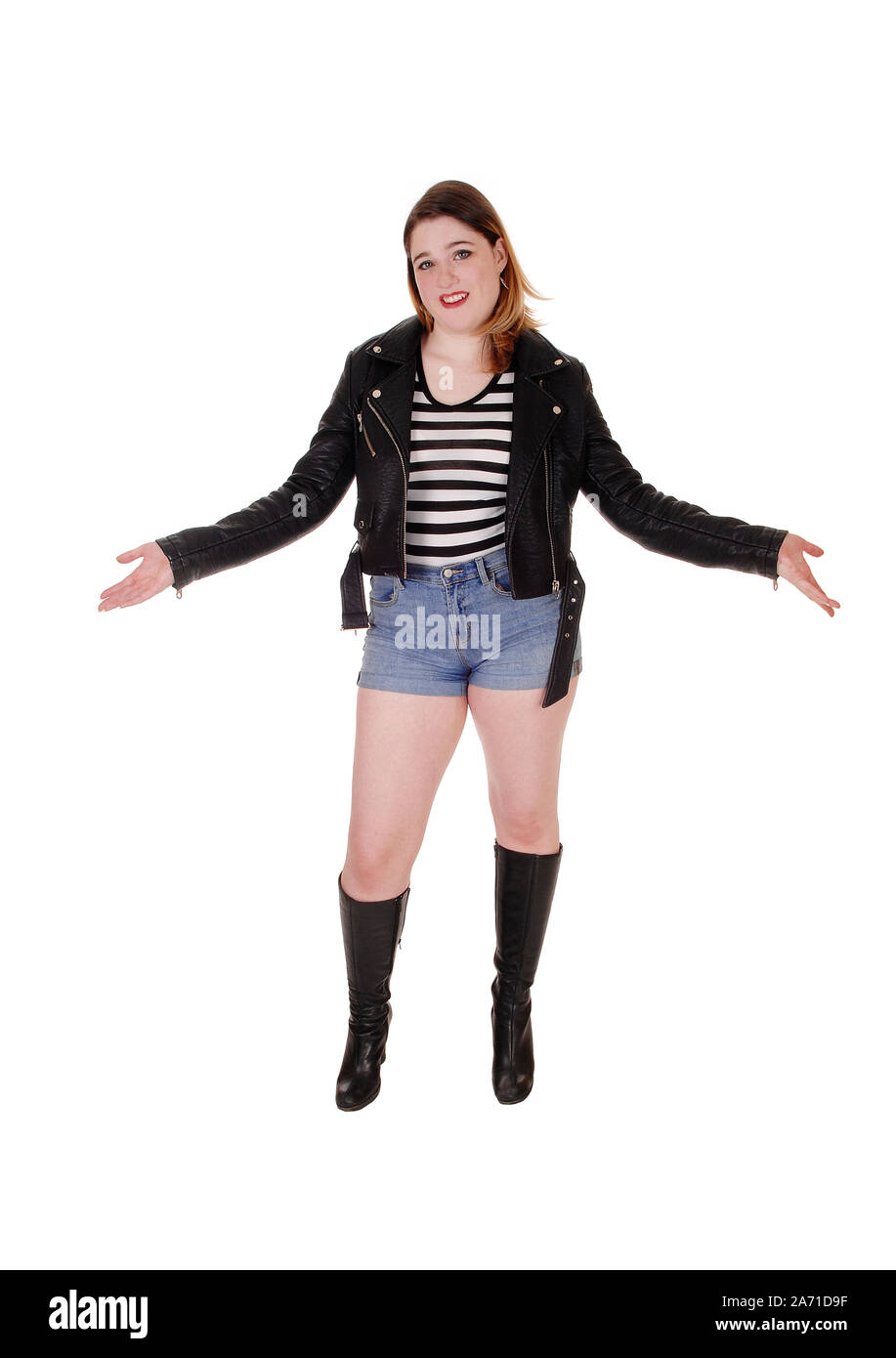 Fashion photo of a beautiful elegant young woman in a pretty leather dress,  bronze-peach metallic boots, thick metal chain around her neck posing over  gray background. Studio shot, portrait. Stock Photo