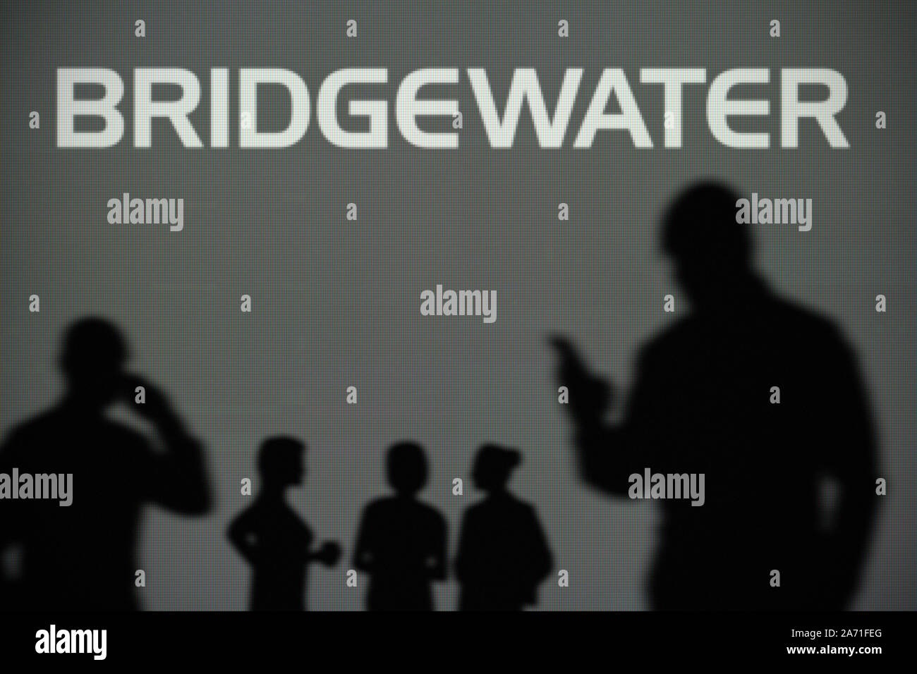 The Bridgewater Associates logo is seen on an LED screen in the background while a silhouetted person uses a smartphone (Editorial use only) Stock Photo