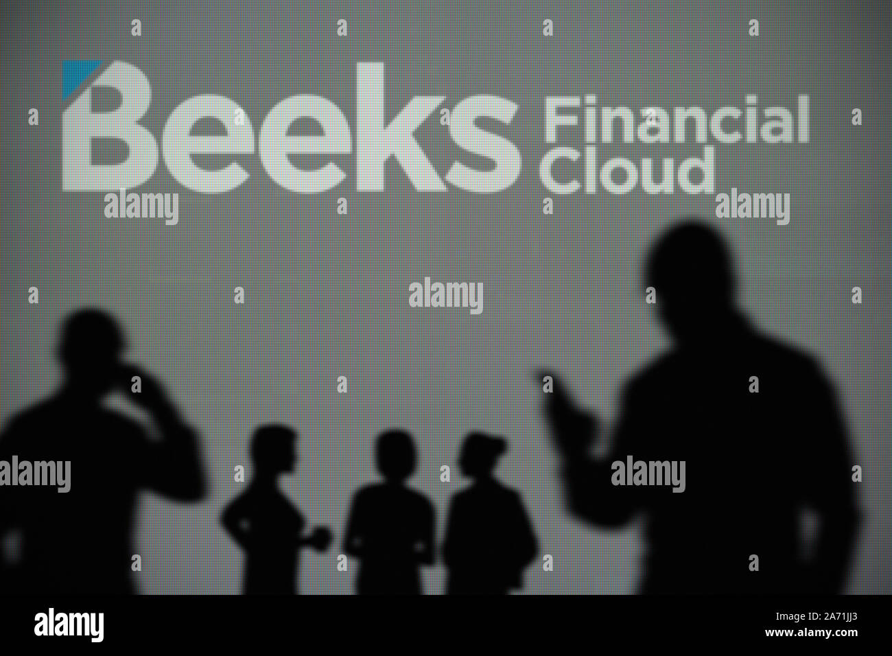 The Beeks Financial Cloud logo is seen on an LED screen in the background while a silhouetted person uses a smartphone (Editorial use only) Stock Photo