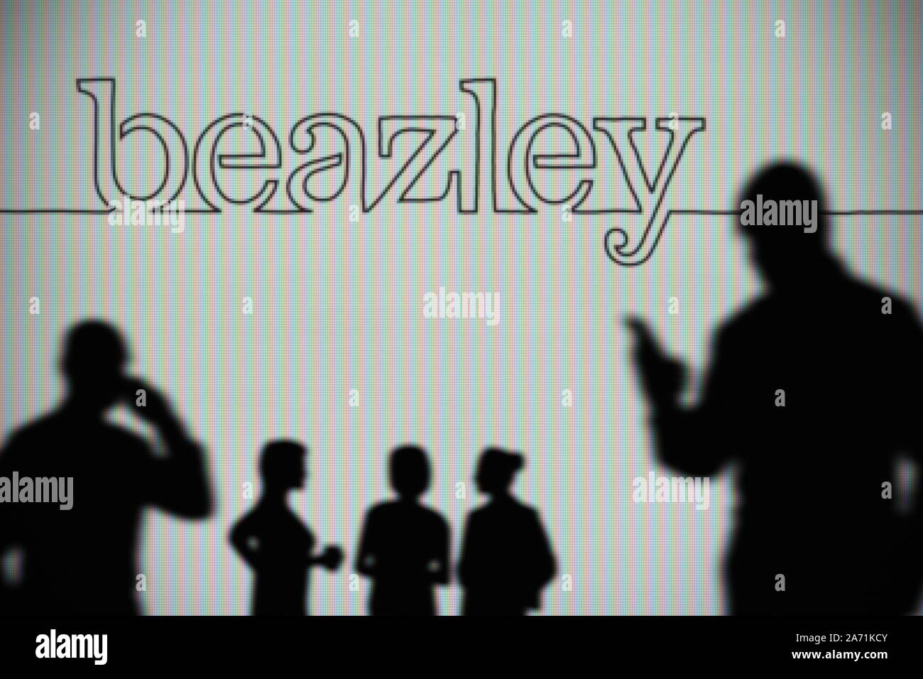 The Beazley Group logo is seen on an LED screen in the background while a silhouetted person uses a smartphone (Editorial use only) Stock Photo