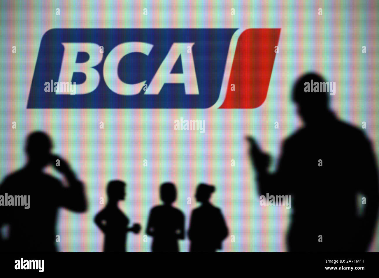 The BCA (British Car Auctions) logo is seen on an LED screen in the background while a silhouetted person uses a smartphone (Editorial use only) Stock Photo