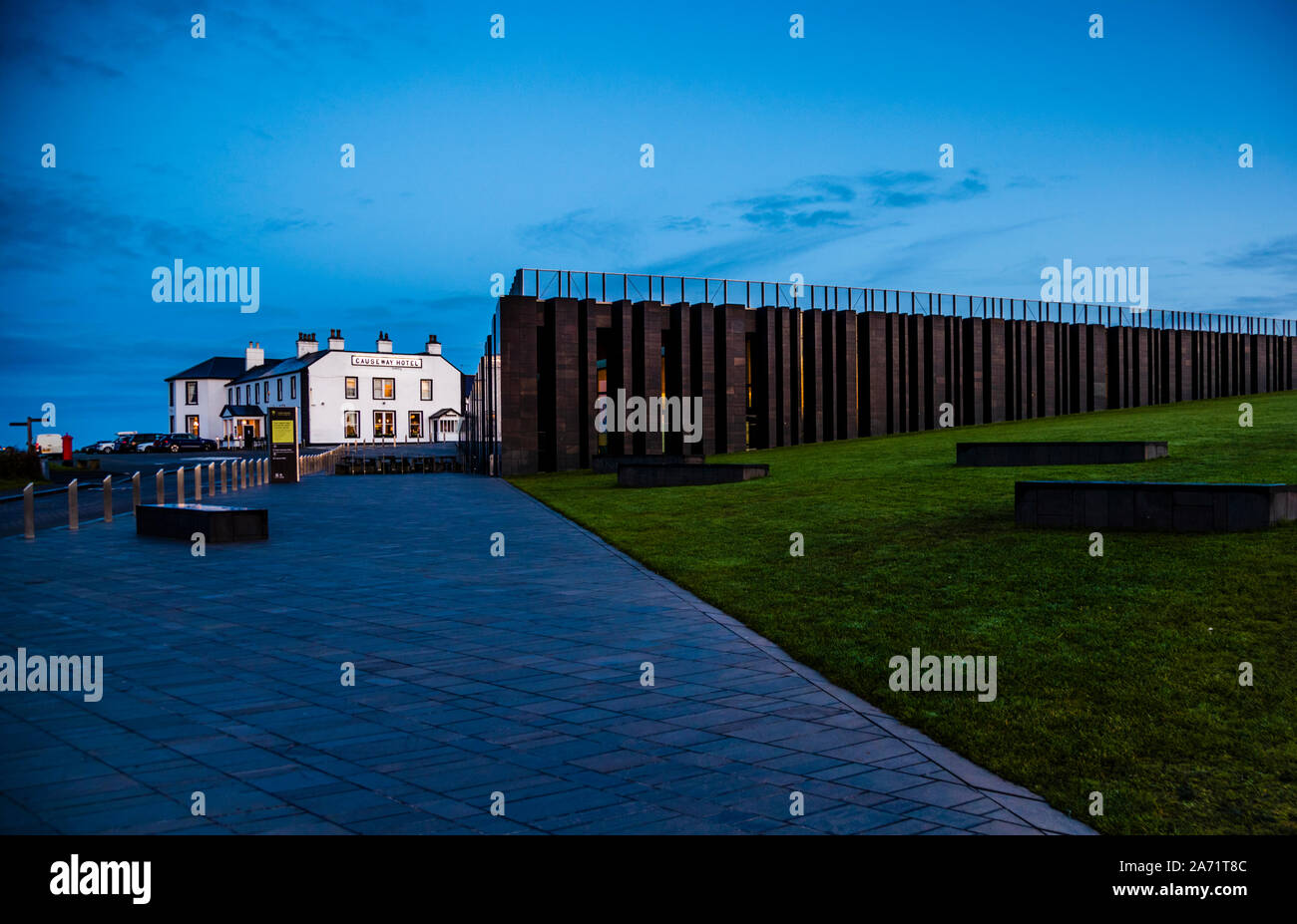 The Causeway Hotel in Bushmills, County Antrim, Northern Ireland, stands at dusk beside the dark, column-like façade of the Giant's Causeway visitor centre. Stock Photo