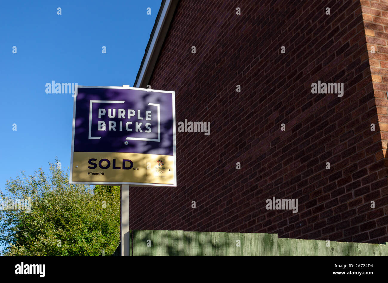PURPLE BRICKS SOLD sign board next to the brick wall of the house. Stock Photo