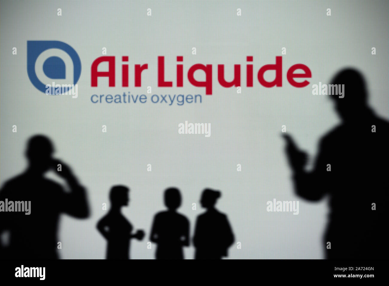 The Air Liquide logo is seen on an LED screen in the background while a silhouetted person uses a smartphone (Editorial use only) Stock Photo