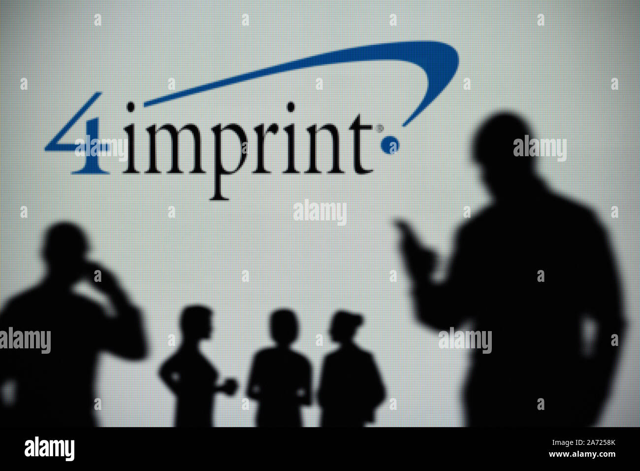 The 4Imprint logo is seen on an LED screen in the background while a silhouetted person uses a smartphone (Editorial use only) Stock Photo