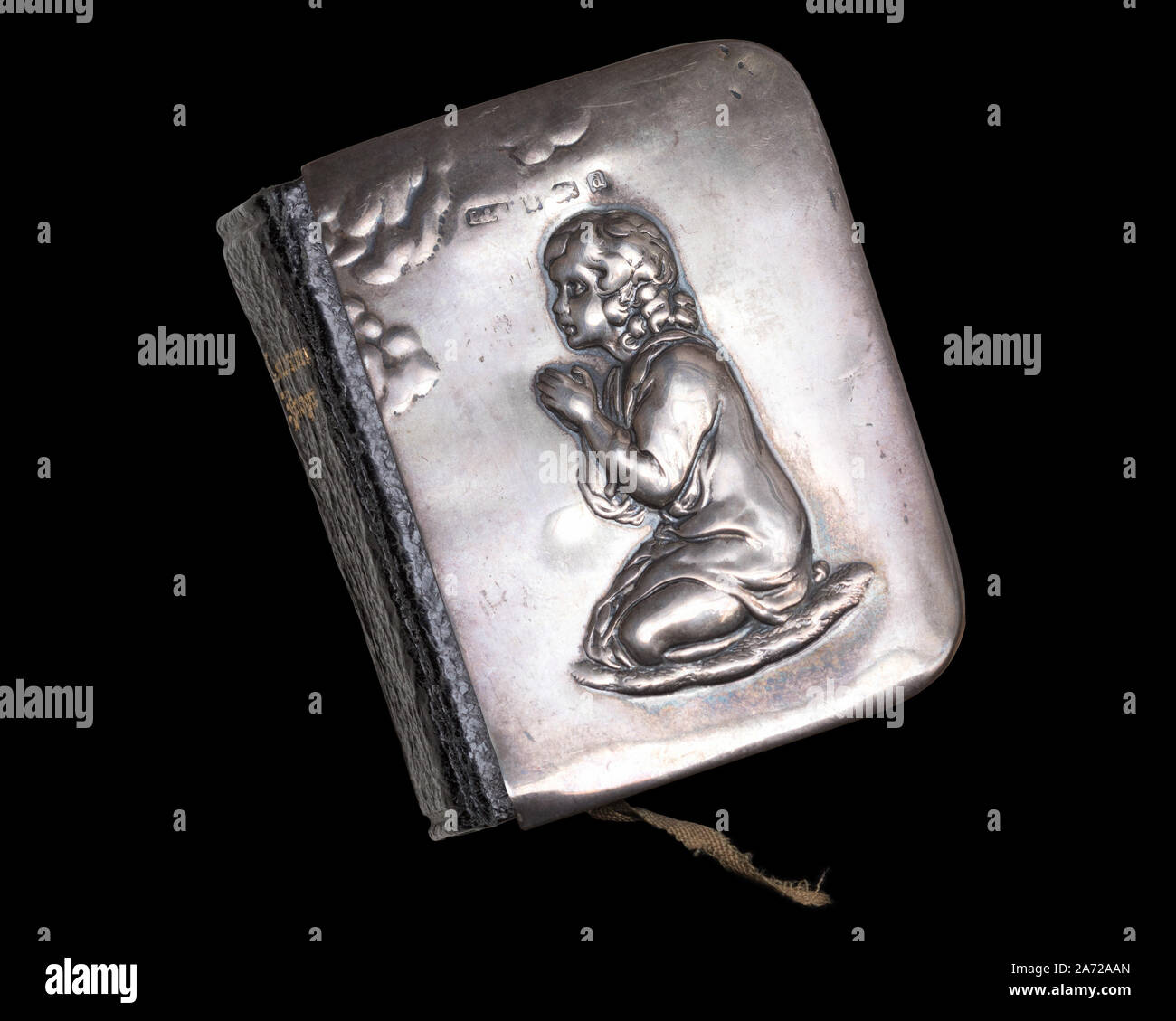 Miniature Edwardian-era Book of Common Prayer with a silver cover depicting a kneeling praying figure in relief, isolated on a black background Stock Photo