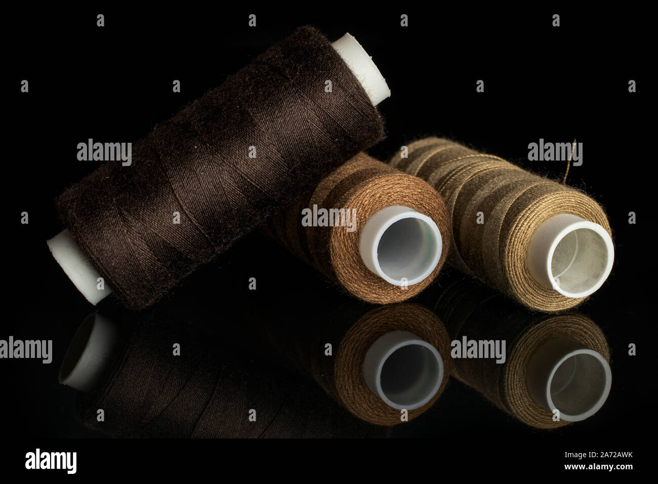 Group of three whole haberdashery item brown thread spools isolated on black glass Stock Photo