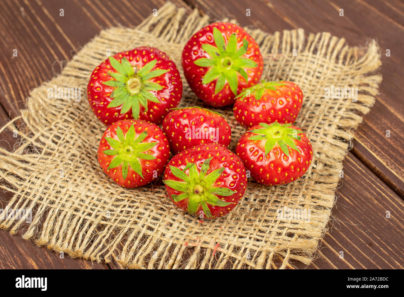 Group of seven whole fresh red strawberry on natural sackcloth on brown ...