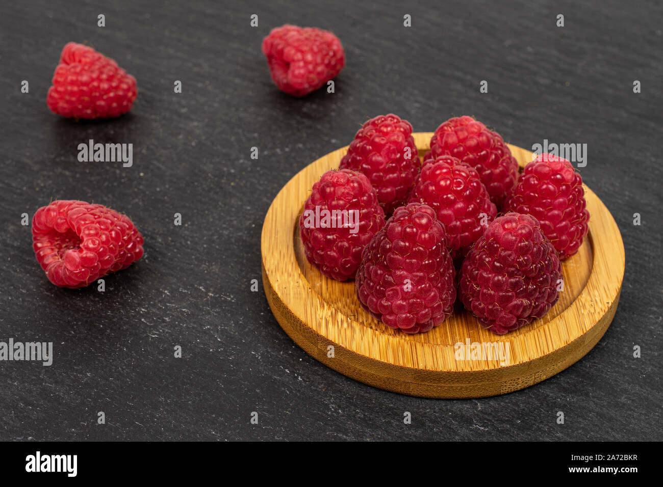 Ten Raspberries Group of ten whole fresh red raspberry on bamboo coaster on grey stone ...