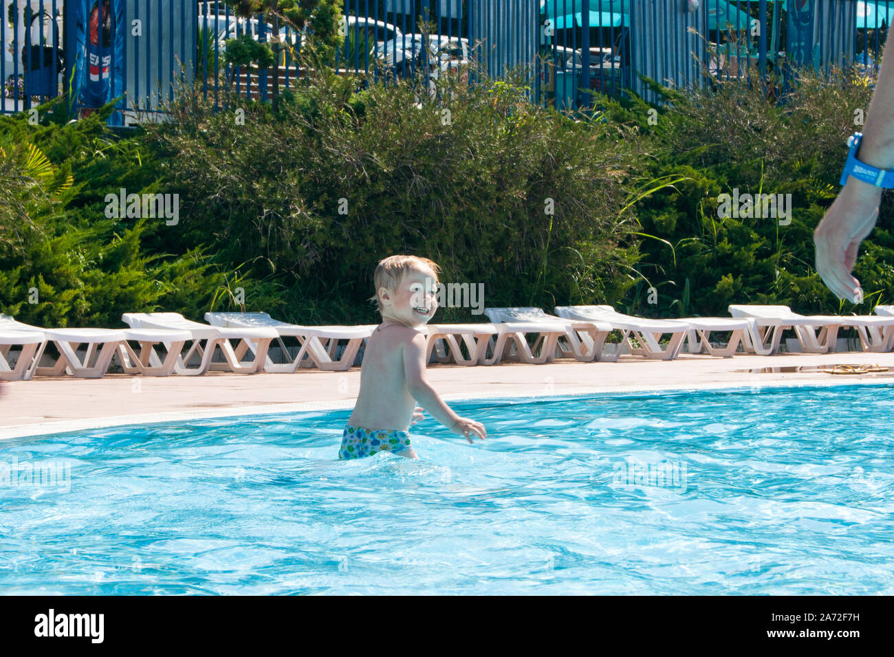 A happy blonde baby of three years with a charred coat is swimming in the children's pool. Stock Photo