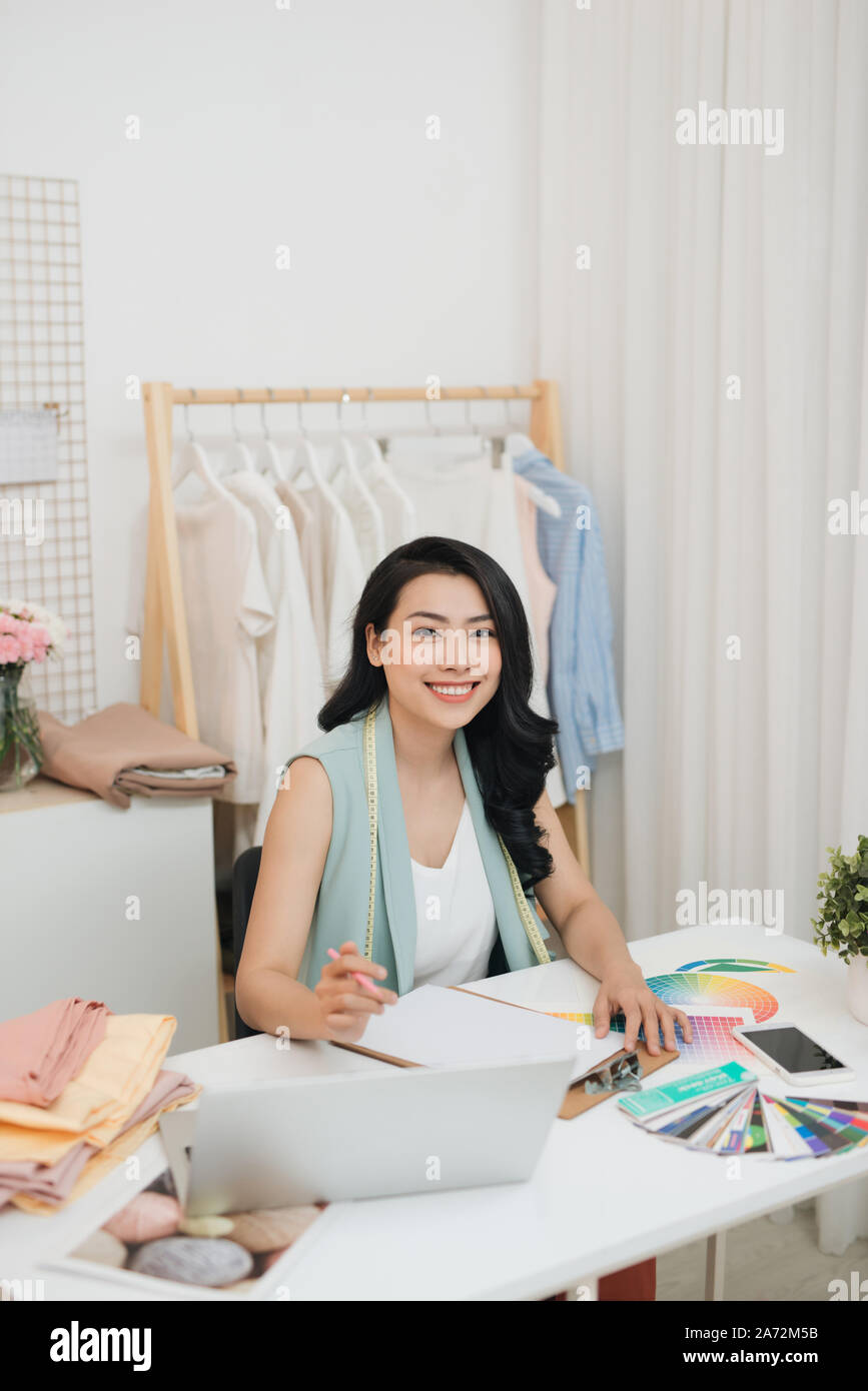 A young Asian fashion designer on her atelier working with a laptop Stock Photo