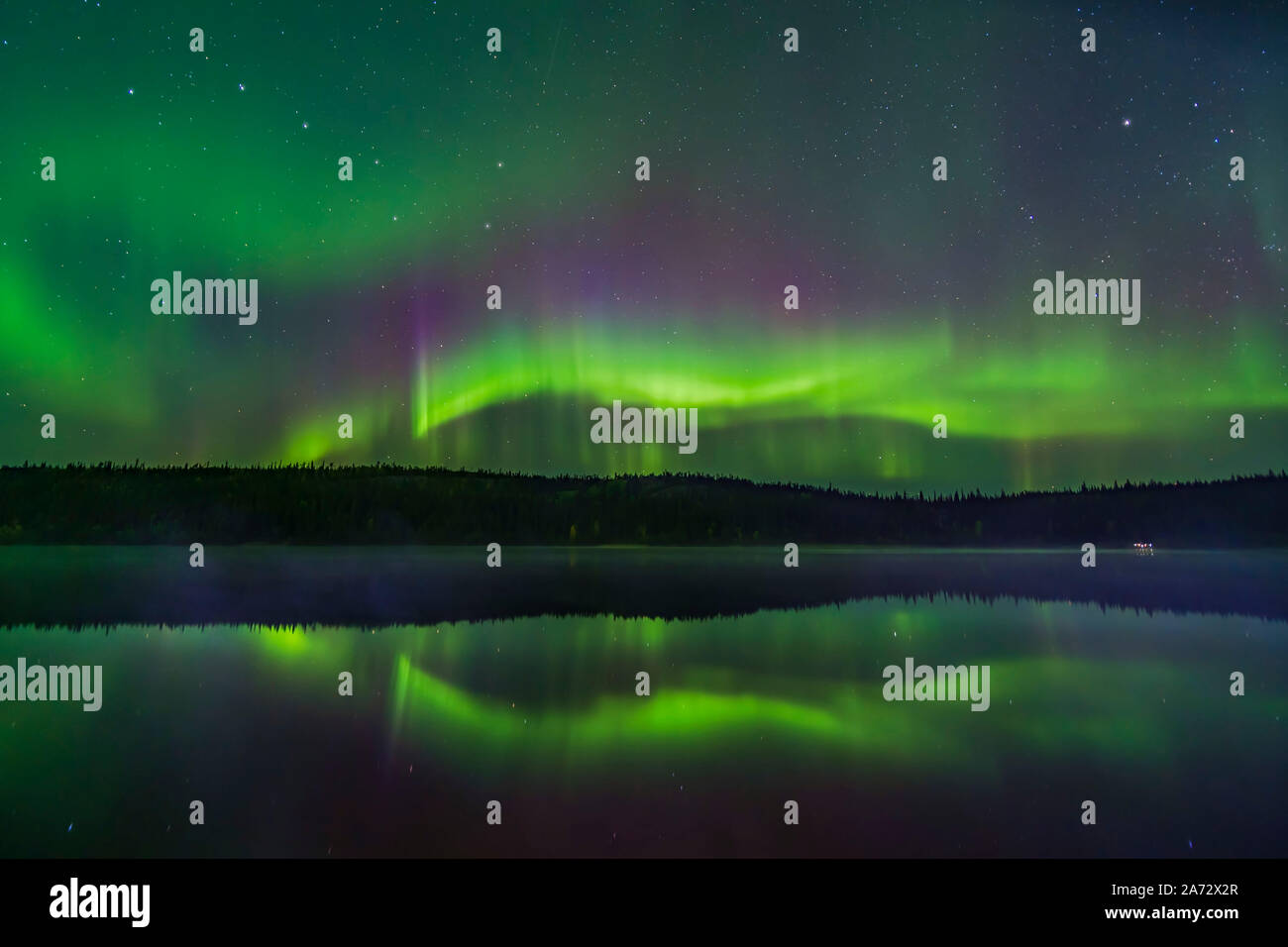 Reflections of the Northern Lights in the calm and misty waters of Madeline Lake on the Ingraham Trail near Yellowknife, NWT on Sept 7, 2019. This is Stock Photo