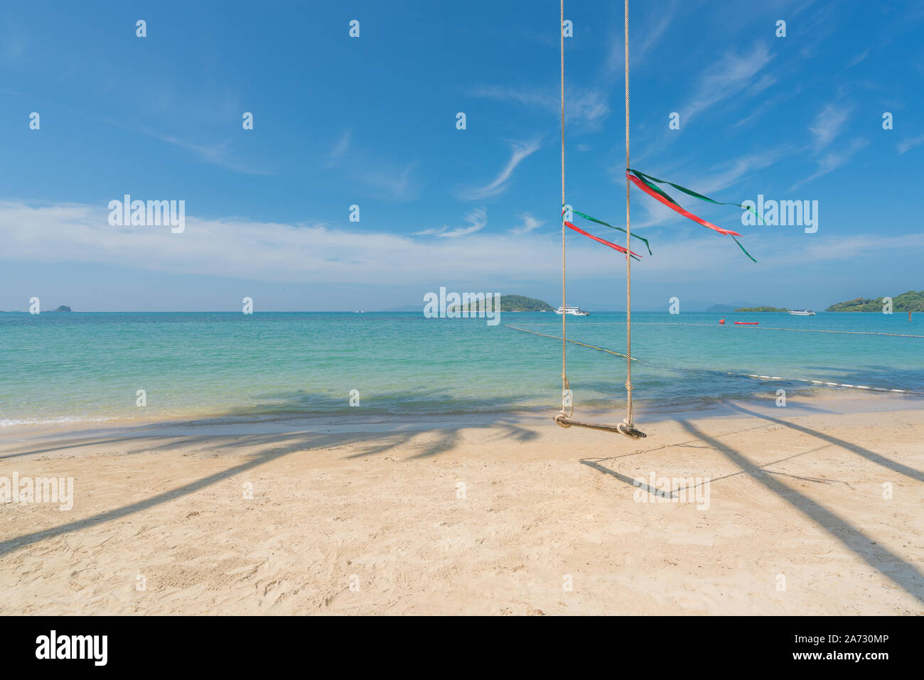 Swing hang from coconut palm tree over summer beach with clear water sea and wave with speed boat in background in Phuket, Thailand. Summer, Travel, V Stock Photo