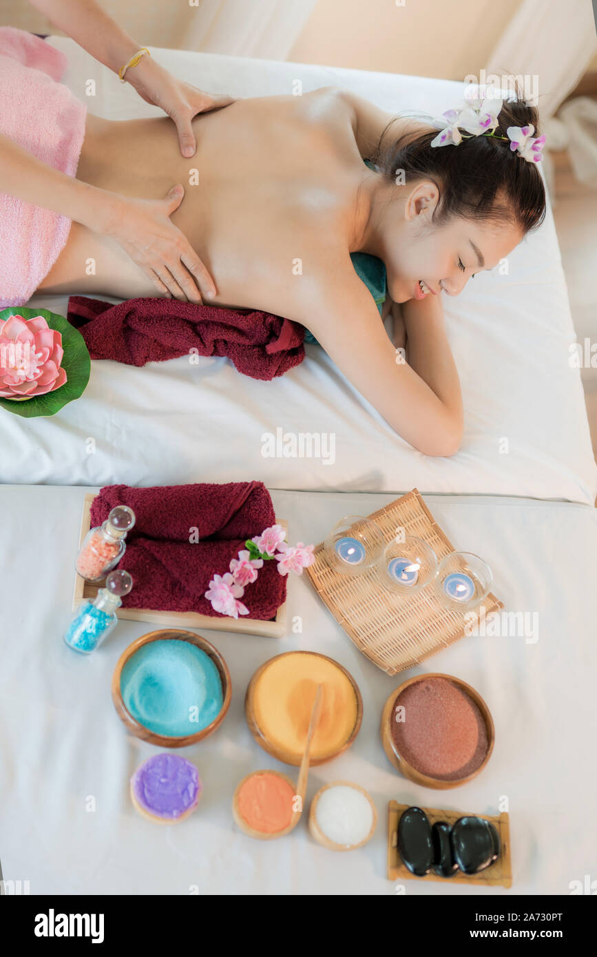 Asian young woman lying on bed and smile having massage and spa salon with spa salt in background  Beauty treatment concept. She is very happy to mass Stock Photo
