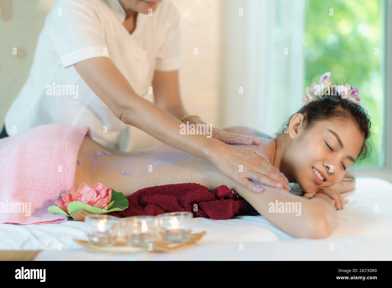 Asian young woman lying on bed and smile having massage and spa salon with spa salt in background  Beauty treatment concept. She is very happy to mass Stock Photo