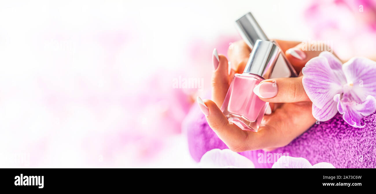 Trendy nail manicure. Woman hands holding nails polishes. Pink decoration from orchids Stock Photo