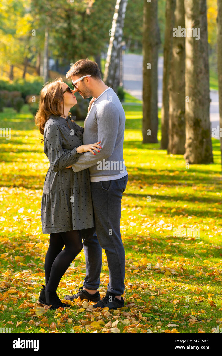 Trendy loving young couple in an autumn park standing in a close embrace looking into each others eyes with love Stock Photo