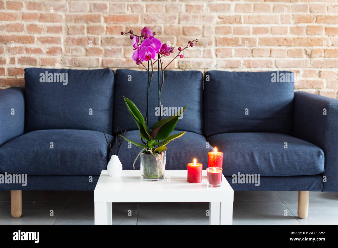 Living room table with orchid flowerpot, candles and air refresher sticks in modern interior design. Stock Photo
