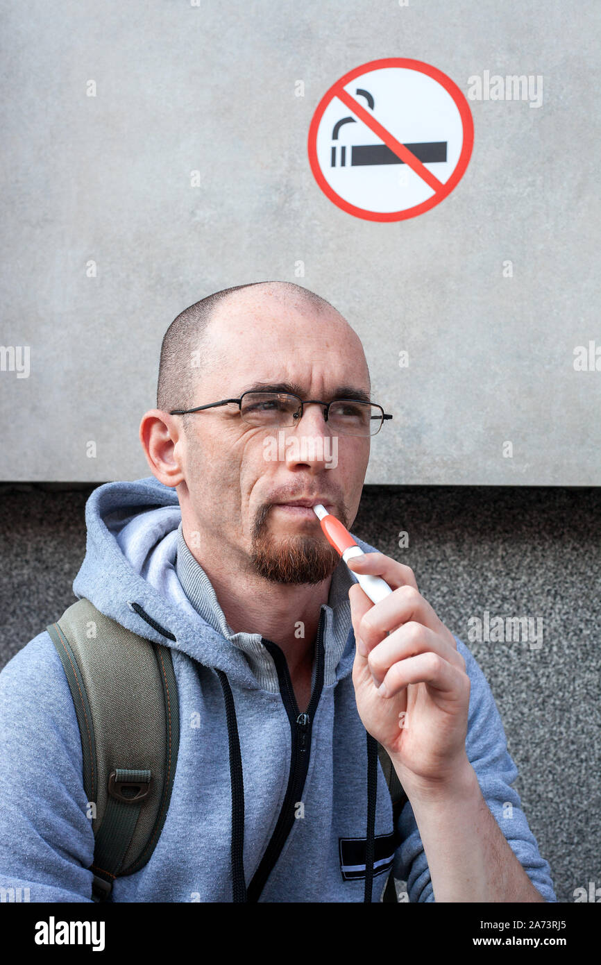 Portrait of caucasian man smoke electronic cigarette under sign No smoking  at city street. Concept violation of rules, Iqos system Stock Photo - Alamy