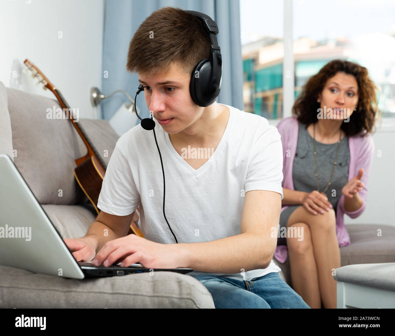 Teenage son listening music in headphones or playing online games ignoring  his mother Stock Photo - Alamy