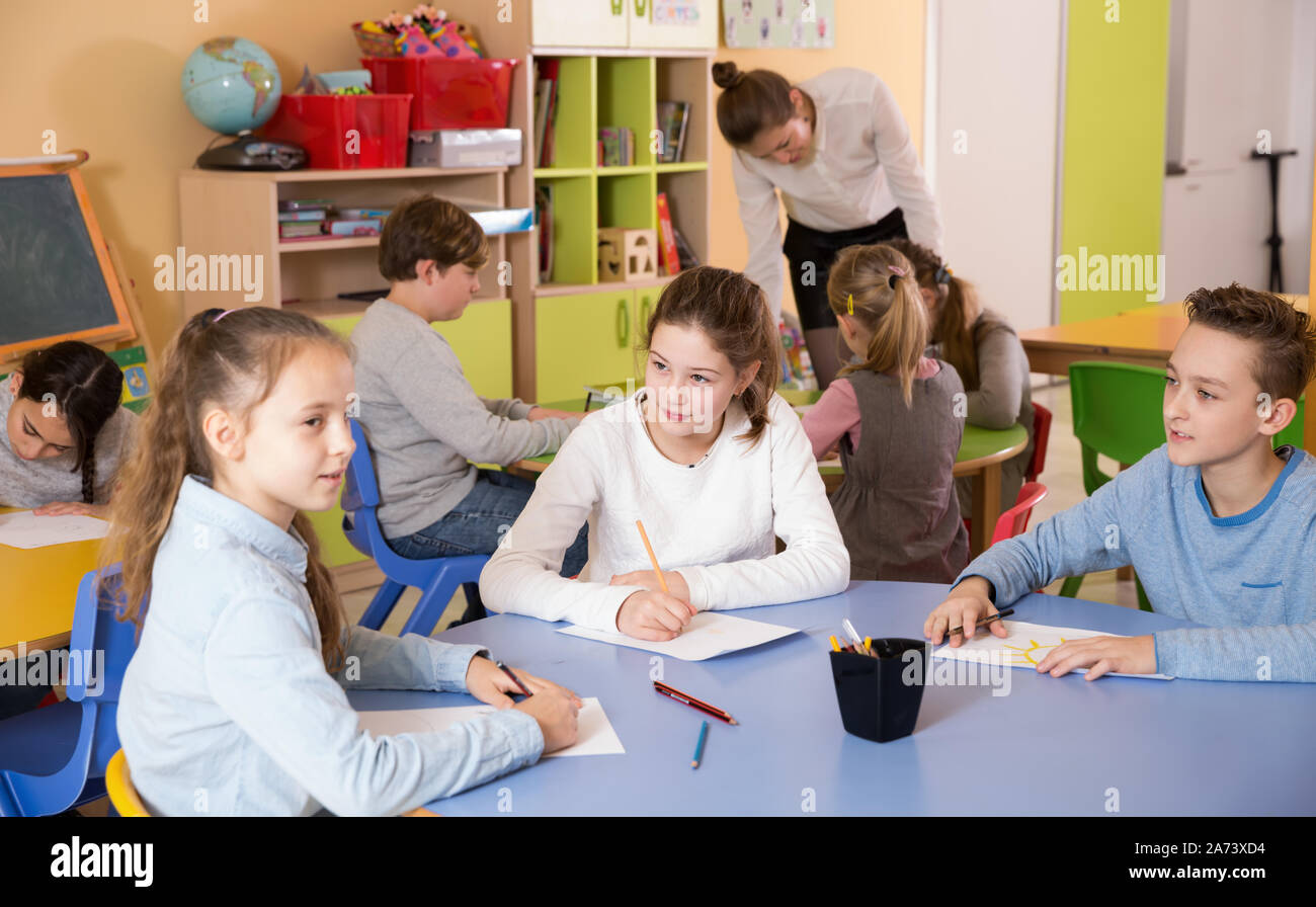 Children elementary age drawing at class, woman teacher helping Stock ...