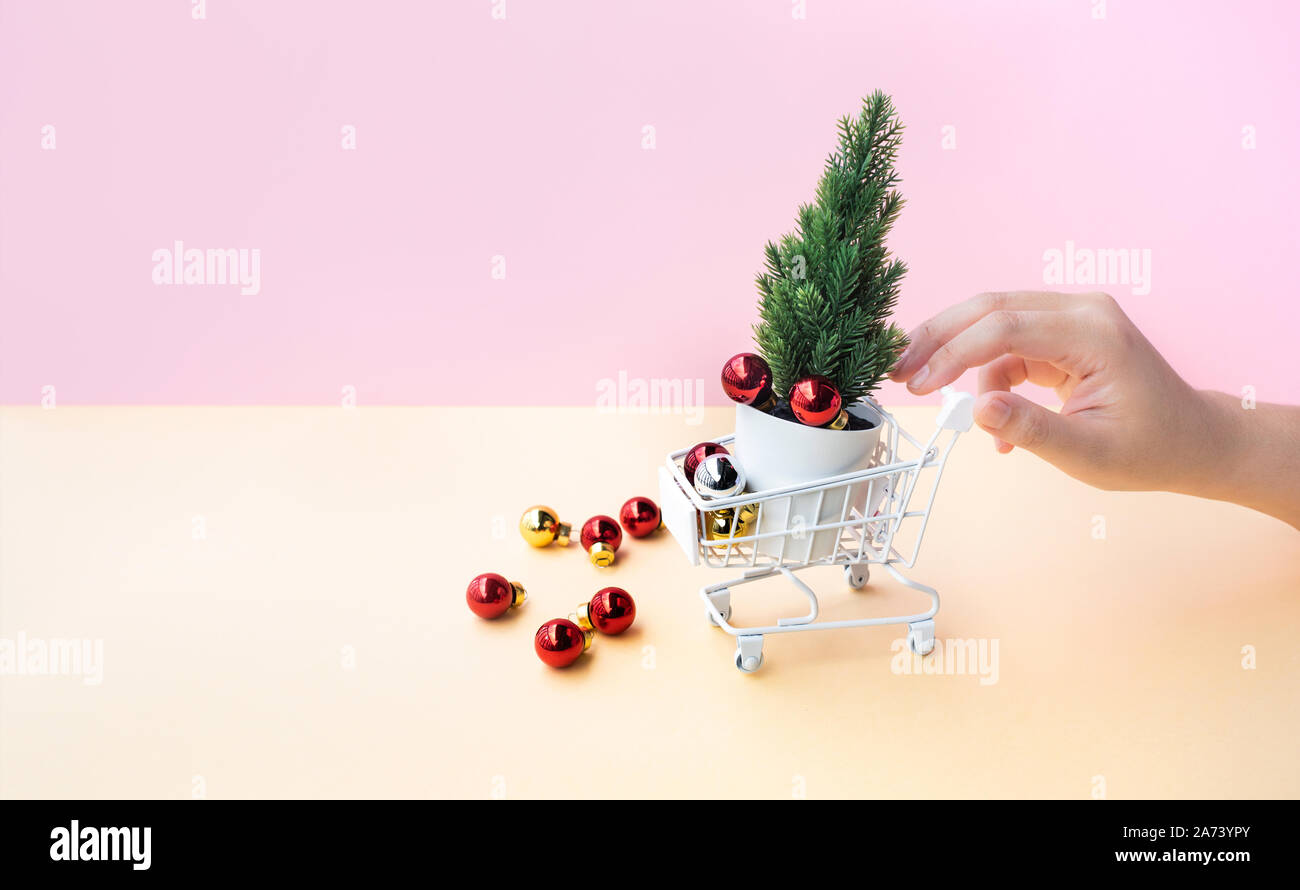 Young woman hand pushing mock up cart,trolley and christmas ornament in side,over all on pastel color background.Celebration festival and online shopp Stock Photo