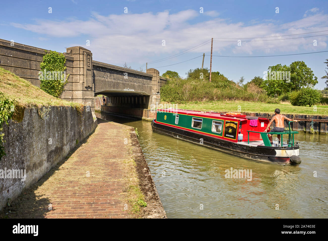 A small hire narrowboat going under a Northampton County Council roadbridge at Stoke Bruerne Stock Photo