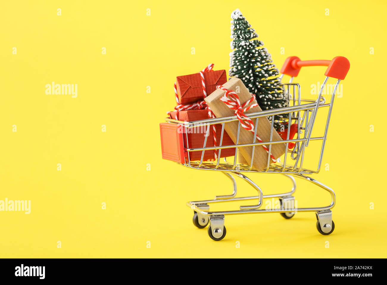 Shopping cart full of various gift boxes and a Christmas tree on yellow background. Christmas sale concept. Stock Photo