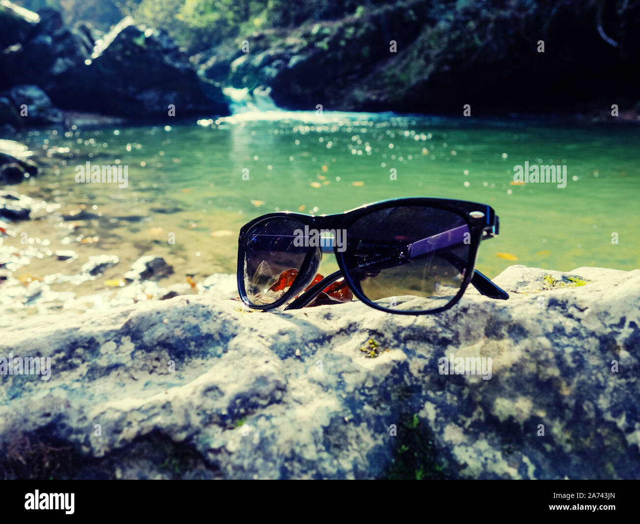 sunglasses on the stone and river view, Beautiful view of mountain river among boxwood trees in autumn Stock Photo