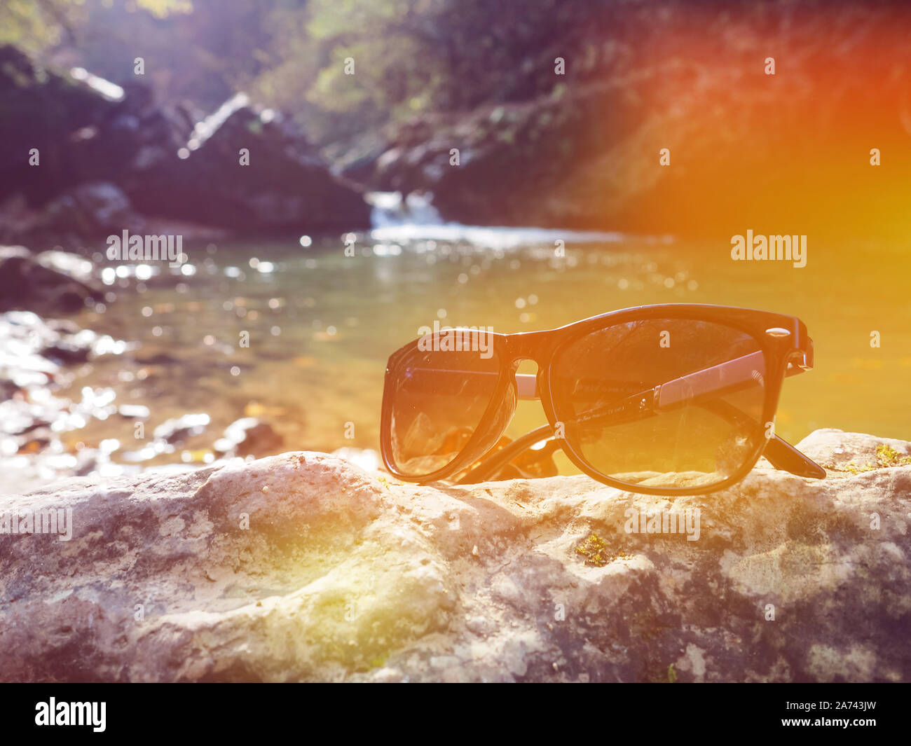 sunglasses on the stone and river view, Beautiful view of mountain river among boxwood trees in autumn Stock Photo