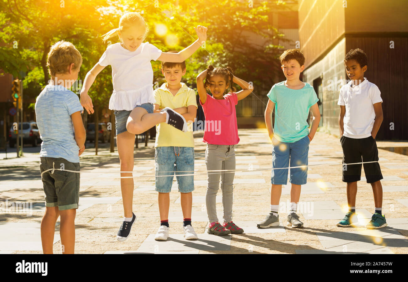 Smiling children playing rubber band jumping game and laughing outdoor