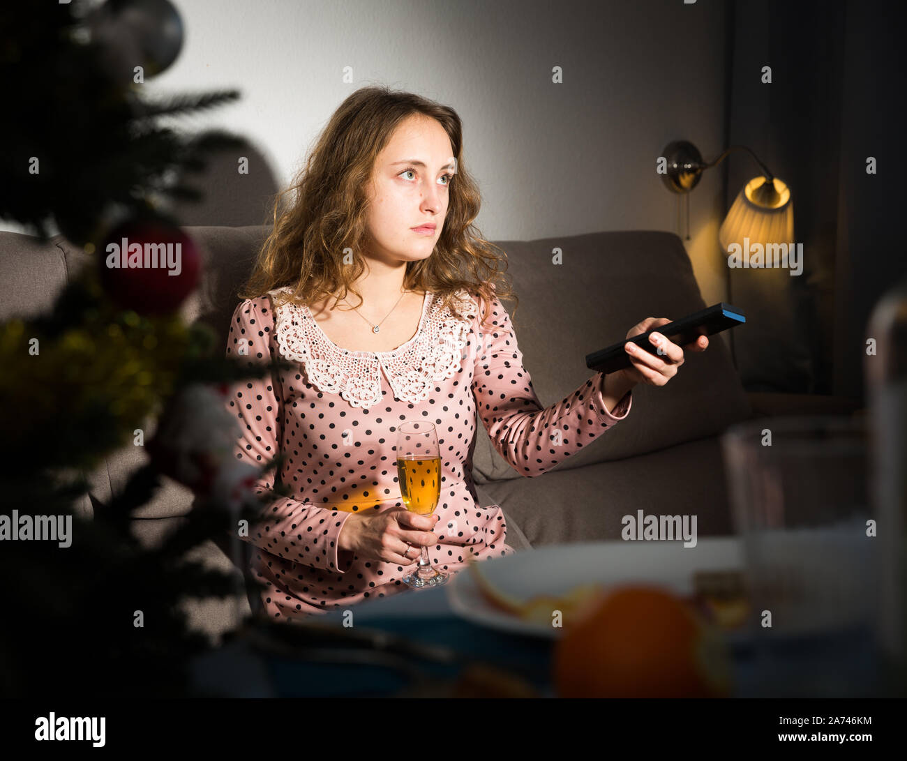 Sad woman sitting at home holding glass of wine and watching tv at ...