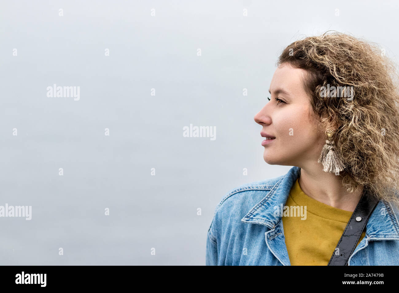 Portrait of a young woman with curly hair looking away dreaming, outdoors. Stock Photo
