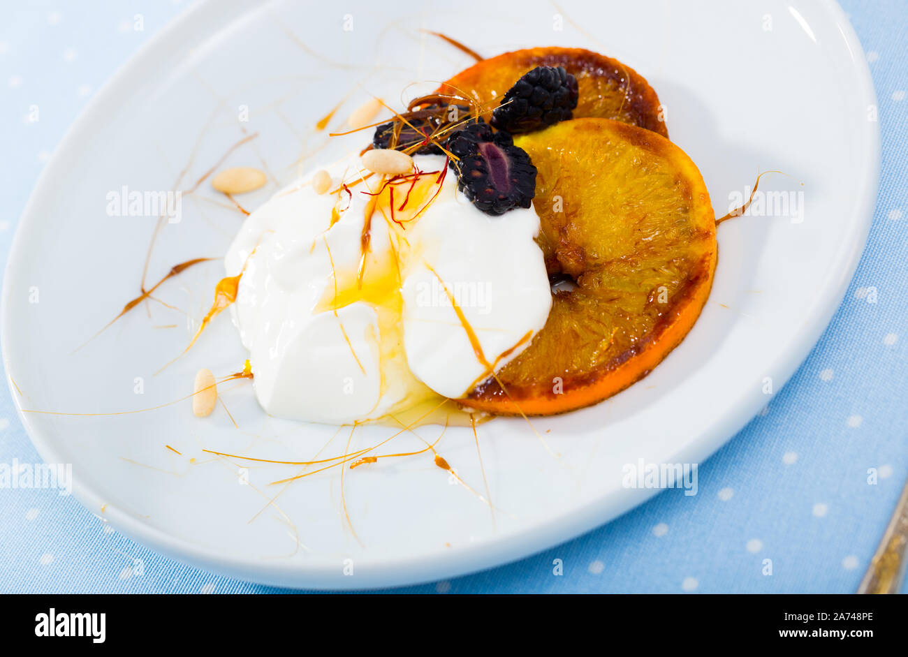 Dessert with sliced caramelized oranges, delicate cream yogurt, fresh brambleberries and pinenuts Stock Photo