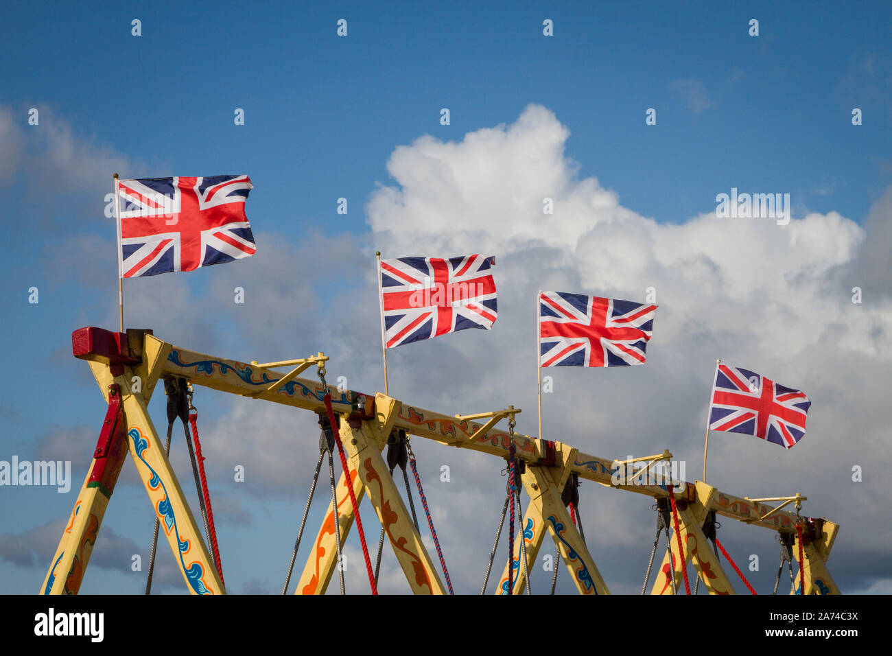 A row of colourful Union Flags on the top of  vintage fairground swings against a bright blue sky Stock Photo