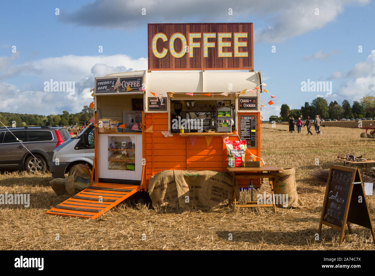 An orange painted horse box converted to a mobile coffee stall at a ploughing match near Ipsden, Oxfordshire with a blue sky and Cumulus clouds Stock Photo