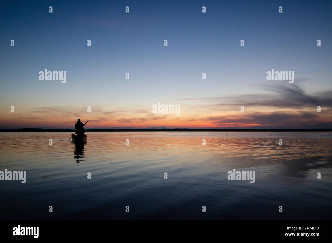 Silhouette of fishing boat and fisherman in the sunrise on the lake in ...
