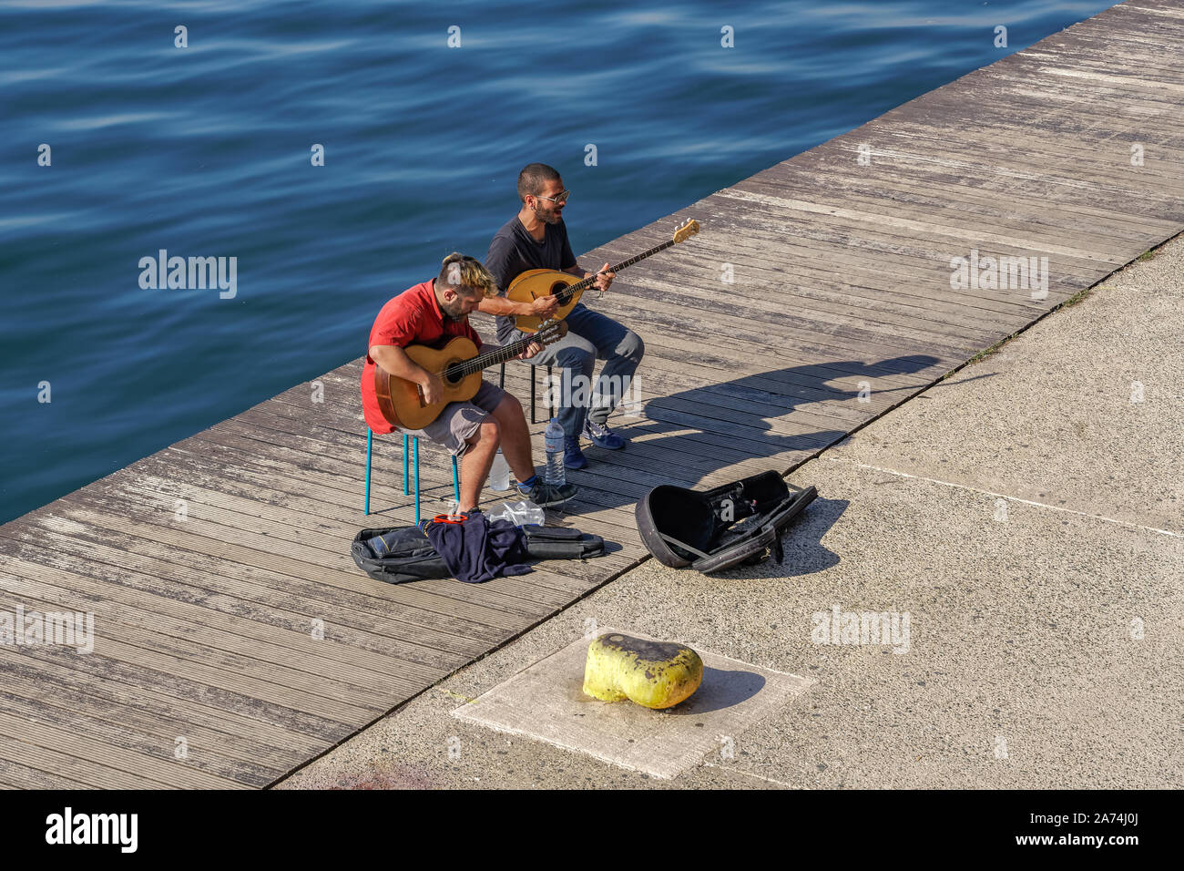 Street musicians performing live music by seafront. Male Greeks playing stringed musical
