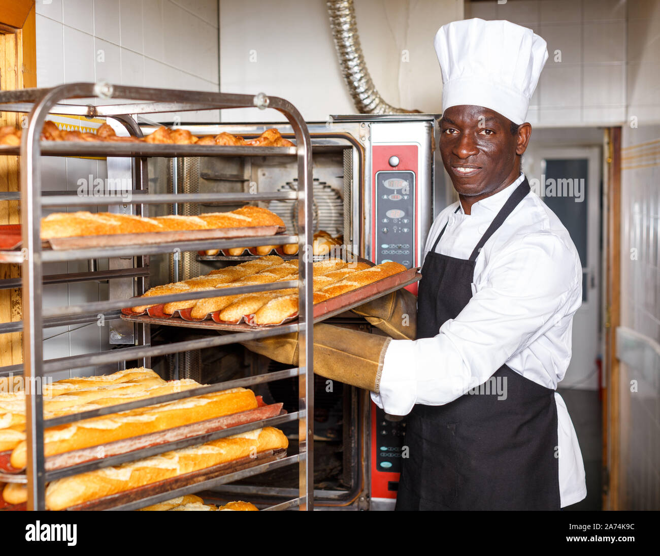 Portrait of African American baker putting fresh baked baguettes on rack at bakery Stock Photo