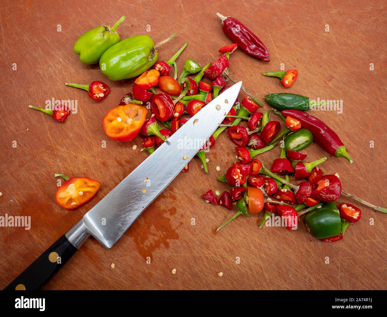 A knife on a chopping board in a kitchen with chopped and cut up red and green chillies Stock Photo