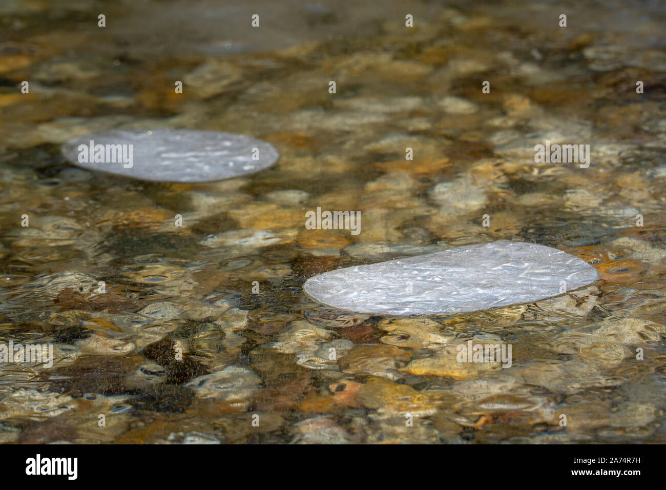 Ice air bubbles stagnated in frozen cold frozen water with colorful stones below. Stock Photo