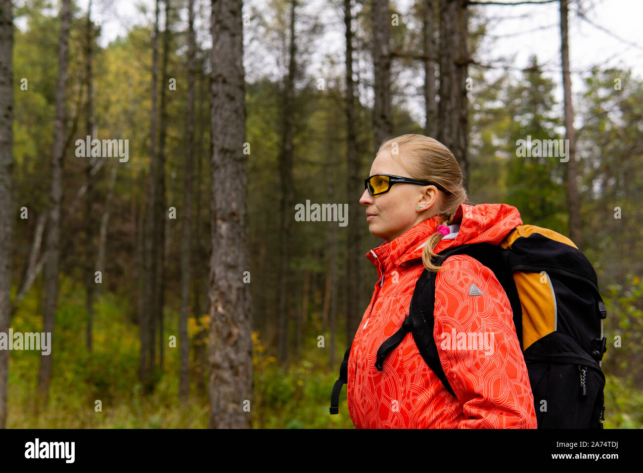 young blonde female hiker with backpack in autumn forest, half-length portrait Stock Photo