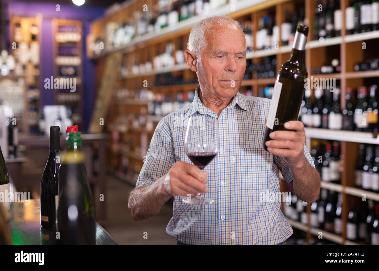 Older man inspecting quality of red wine in wine store in search of