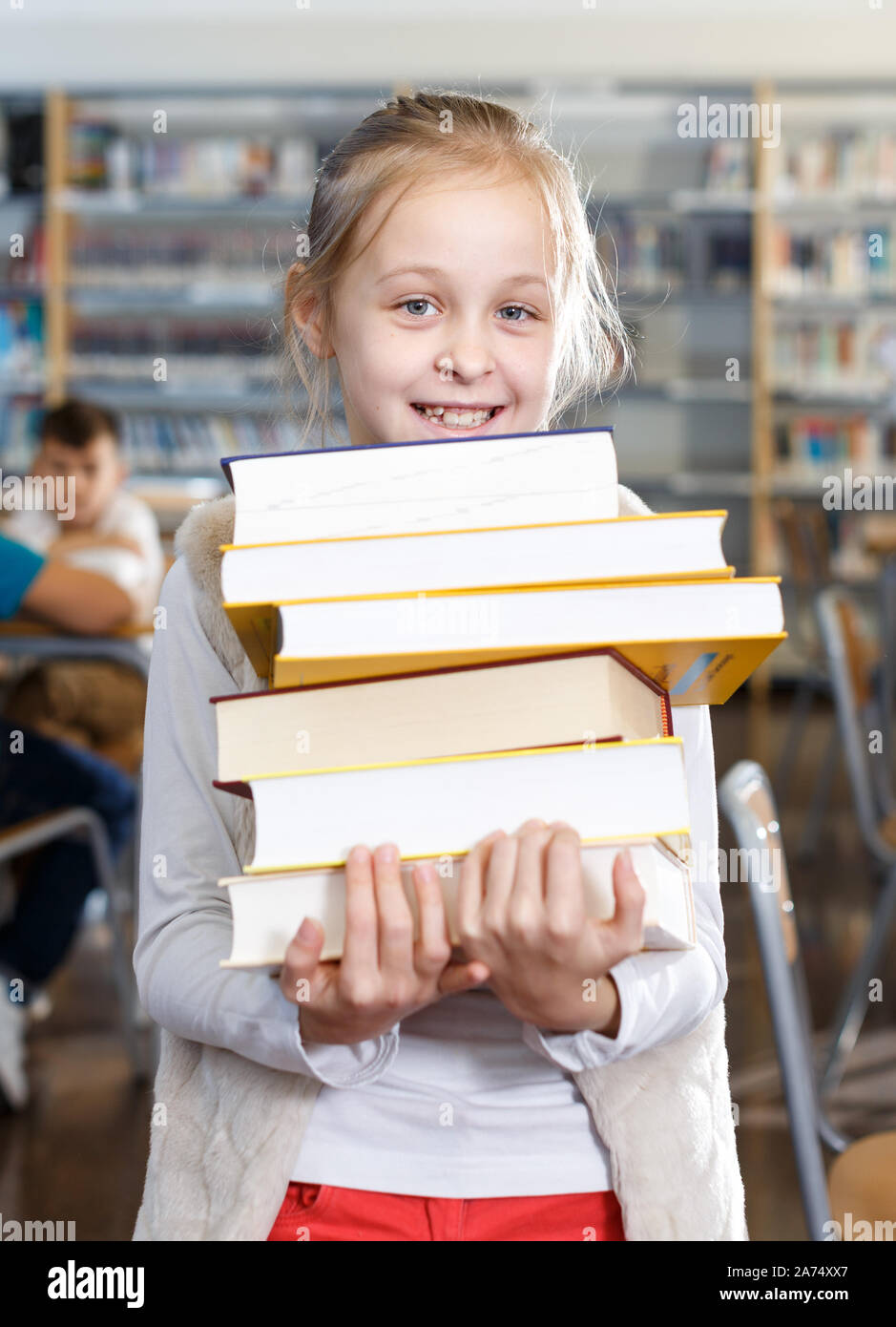 Portrait of smiling teen girl standing with pile of books in school ...