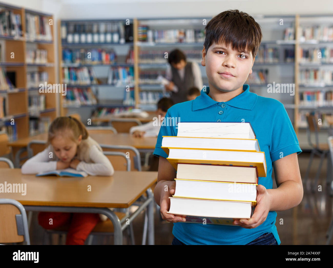 Portrait of smiling preteen boy standing with pile of books in school ...