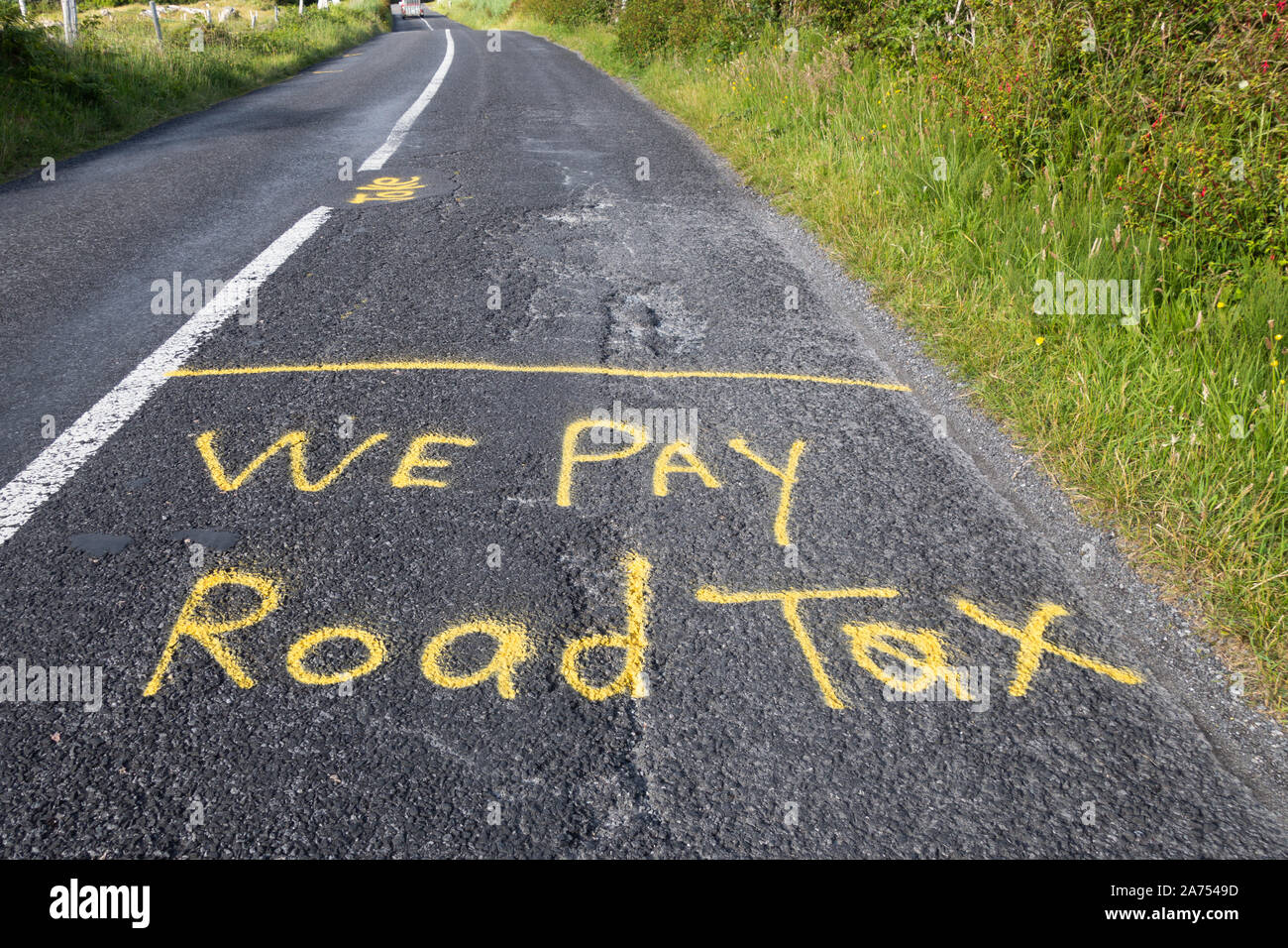 Protest signs spray painted onto the road in Ireland complaining about the poor upkeep of the Roads. We Pay Road Tax Stock Photo